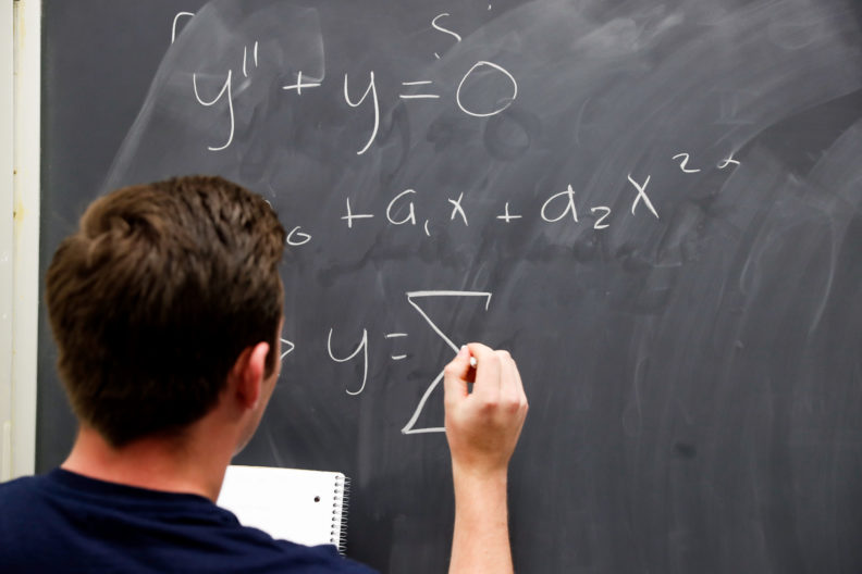 An Elmhurst College student writes a mathematical equation on a chalkboard in class.