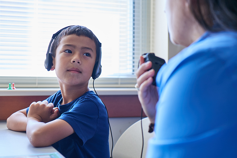 A young boy wearing headphones looks at a speech pathologist in Elmhurst College's Speech Language Hearing Clinic.