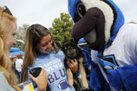 At Elmhurst College Homecoming 2019, an alumna cradles a puppy while mascot Victor E. Bluejay looks on.