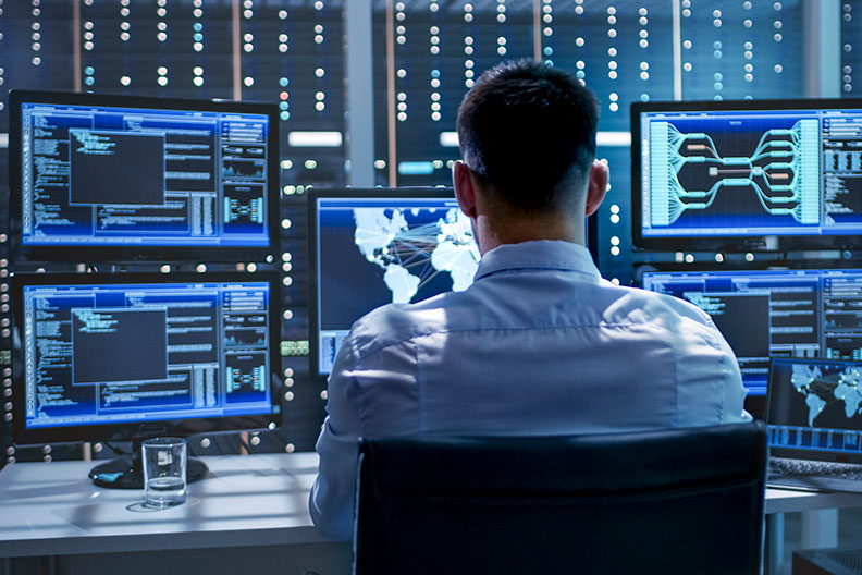 A seated man views multiple computer screens to illustrate the new Elmhurst College cybersecurity major.