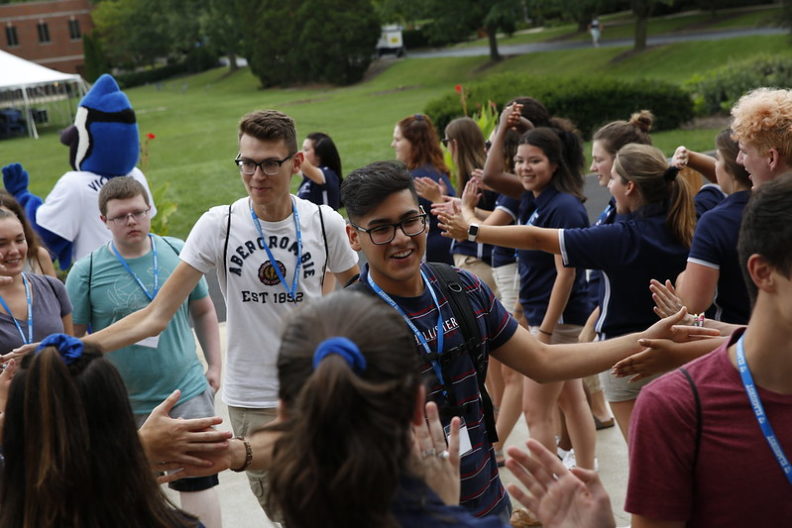 A crowd of Elmhurst University students welcomes new first-year and transfer students to campus with high-fives and handshakes.