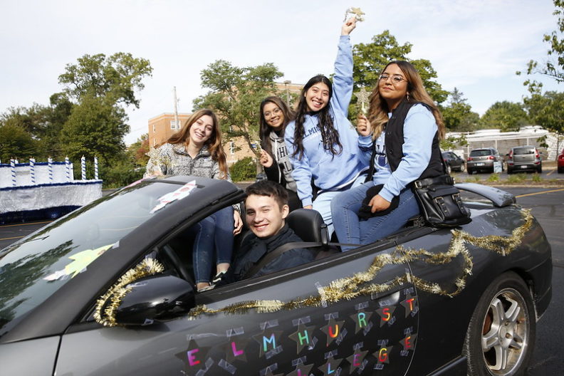 A group of Elmhurst University students sitting in a convertible cheer during the annual Homecoming parade.