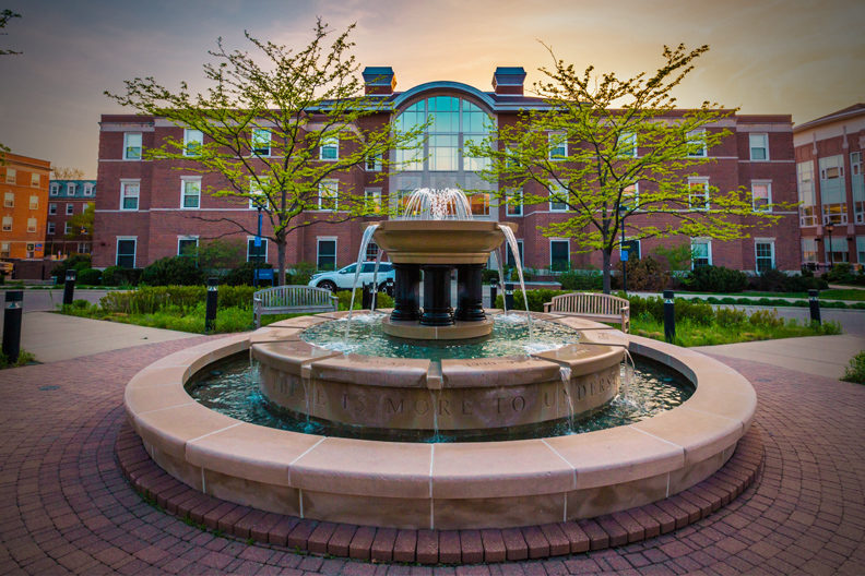 Water pours from the top of the fountain on the campus of Elmhurst University, with Circle Hall in the background.