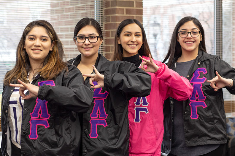 Four Latina students make the sign of their sorority.