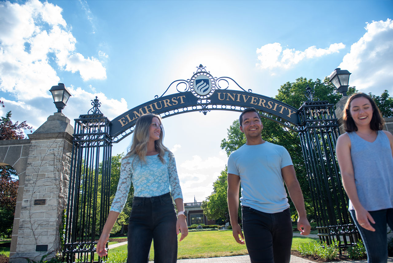 A female student and a male student at Elmhurst University walk beneath the Gates of Knowledge on campus.