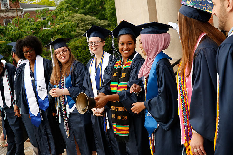 A diverse group of honor graduates stand together and ring a ceremonial bell during Elmhurst University's 2019 Commencement ceremony.
