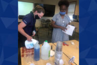 Two Elmhurst University faculty members standing over a table prepare STEM kits for students.