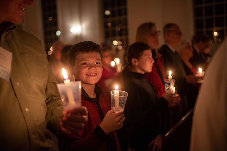 A smiling boy holds a candle in the audience of the Elmhurst University Festival of Lessons and Carols.