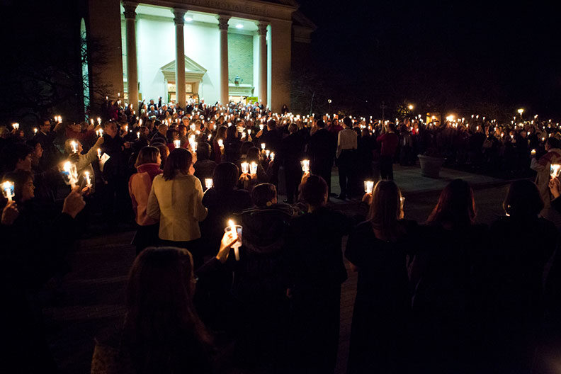The audience stands and holds candles in the darkened Hammerschmidt Memorial Chapel during the Elmhurst University Festival of Lessons and Carols.