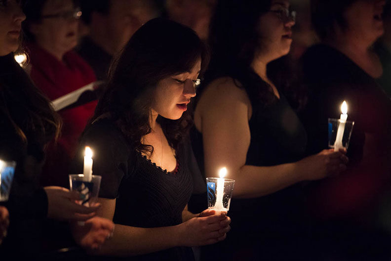A female member of the Elmhurst University choir sings while holding a candle during the annual Festival of Lessons and Carols.