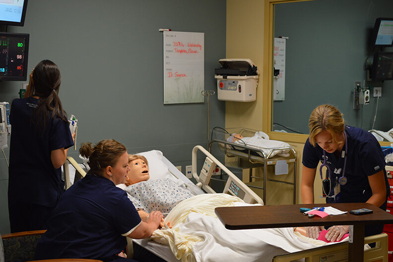 A photo of nursing students working by a hospital bed inside the Elmhurst University Simulation Center at Elmhurst Hospital in Elmhurst, IL.