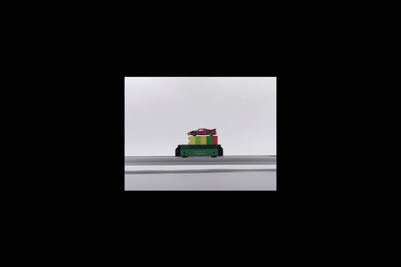 A photo of a toy car on top of a stack of toy blocks on top of a motorized rail..