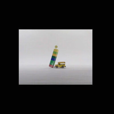 A photo of a toy car colliding with a tower of Lego bricks with a ball resting atop the tower.