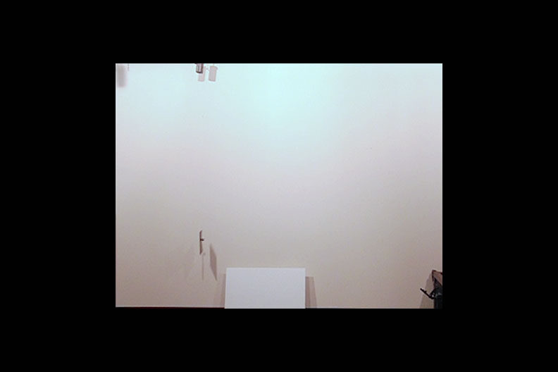 A photo of a white wall with a ball launcher in the lower right corner.