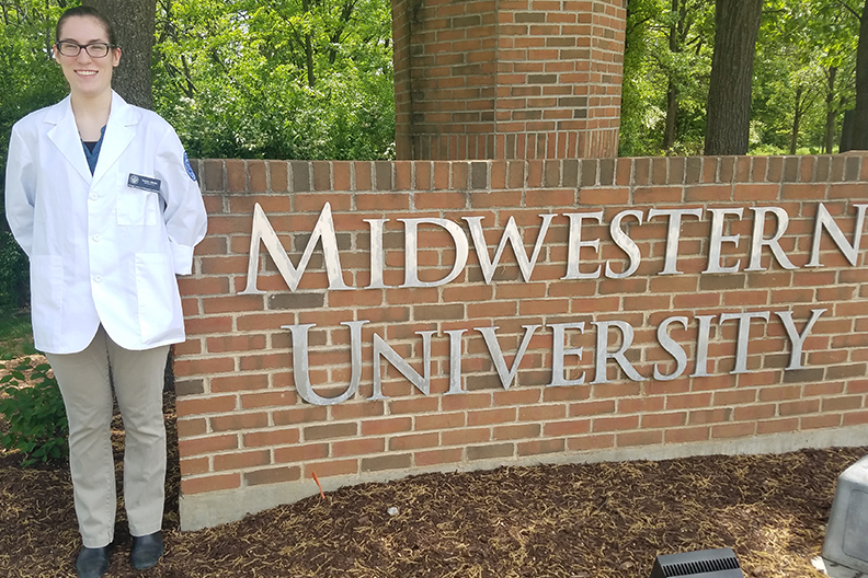 Katie Martin stands in front of a brick sign reading "Midwest University."