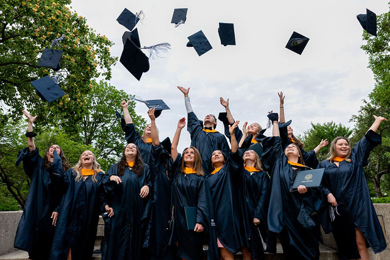 A large group of Elmhurst University graduate students throws their hats up into the air to celebrate their graduation after the 2021 Commencement ceremony.