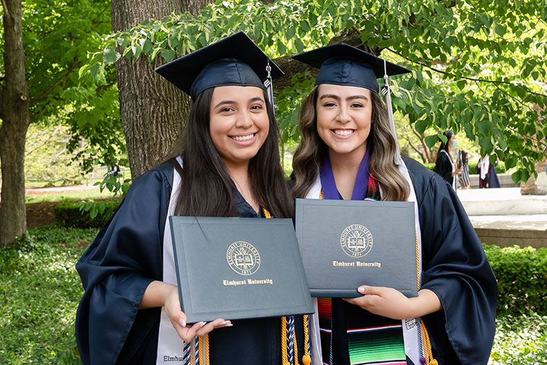 Two female Elmhurst University graduates hold up their degrees following the 2021 Commencement ceremony.