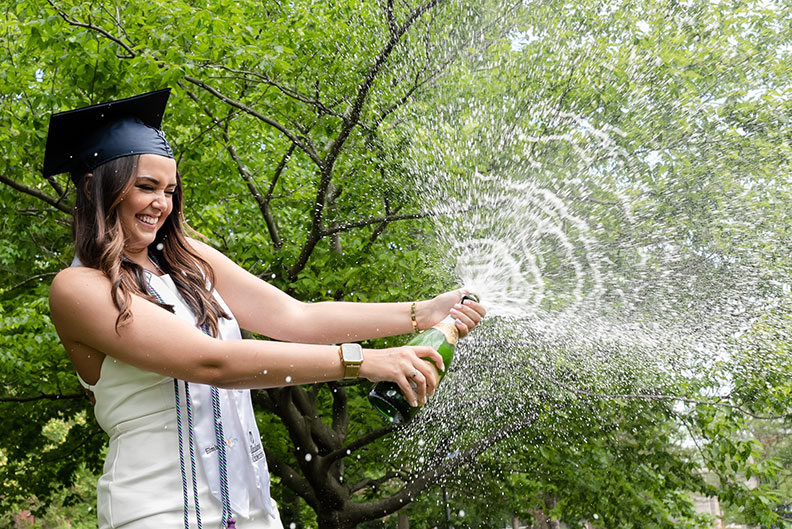 A female Elmhurst University graduate pops open a bottle of champagne following the 2021 Commencement ceremony.