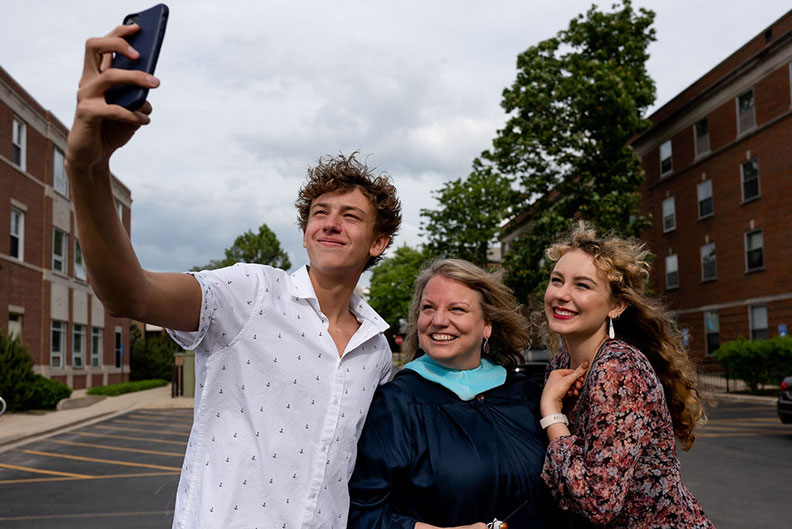 An Elmhurst University graduate student poses for a selfie with others after the 2021 Commencement ceremony.