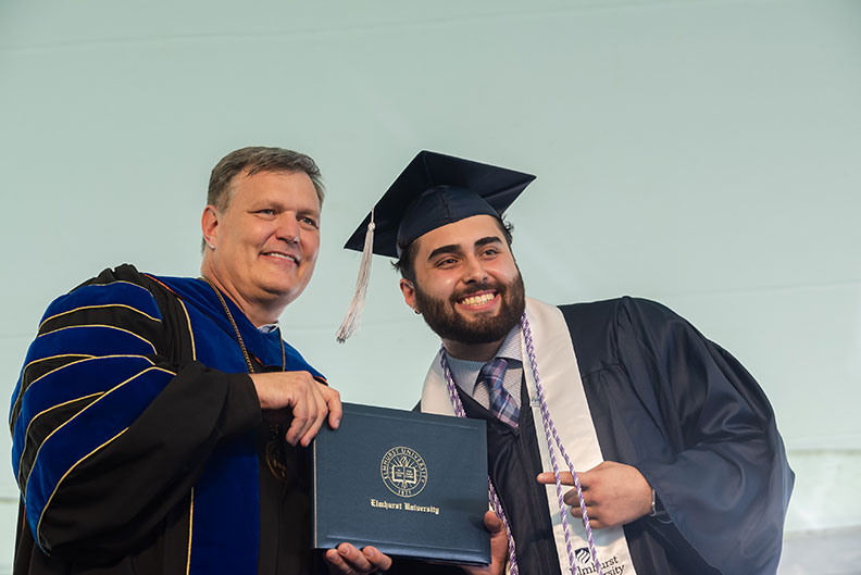 A male Elmhurst University graduate receives his degree onstage during the 2021 Commencement ceremony.