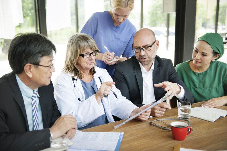 A group of DNP nurses discuss medical findings at a conference room table.