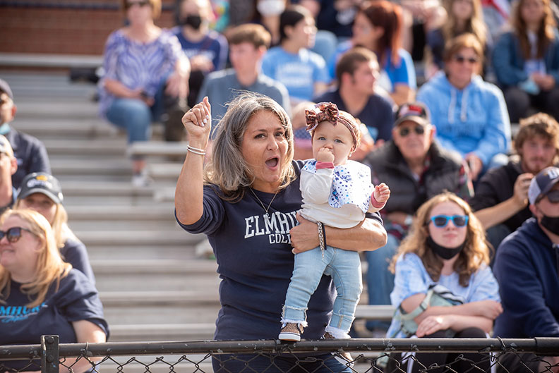 A woman holding a baby girl cheers on the Elmhurst University football team at the 2021 Homecoming game.