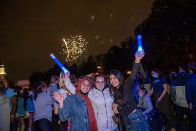 Three female students pose for a photo as fireworks go off in the distance during Elmhurst University's 2021 Homecoming pep rally.