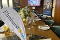 A long dinner table with place settings and an "Elmhurst 150" banner in the foreground.