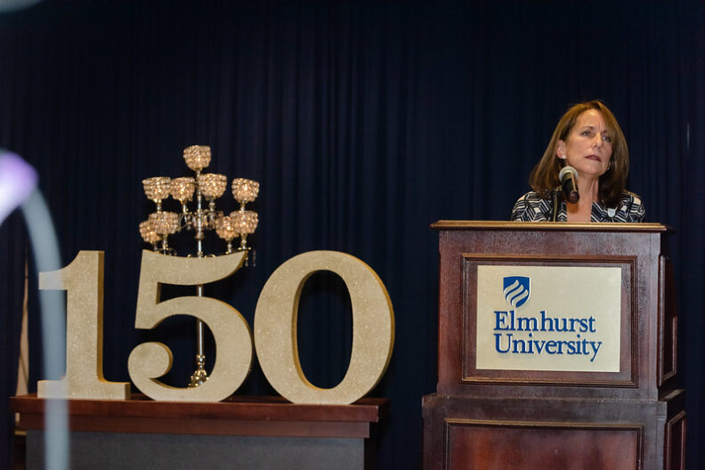 Elmhurst University business department co-chair Shaheen Wolff speaks, with a large number "150" beside her, during Elmhurst's Founders Day celebration.