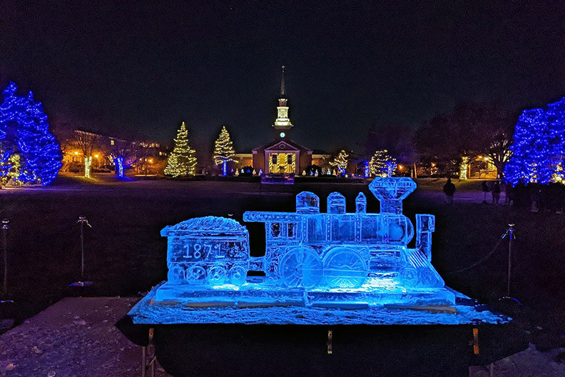 Elmhurst University Mall lit up with holiday lights, and an ice sculpture of a train to celebrate the University's sesquicentennial in the foreground.