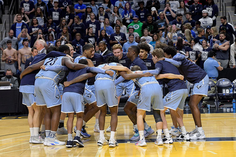 The Elmhurst University men's basketball team gathers in a huddle together on a basketball court.