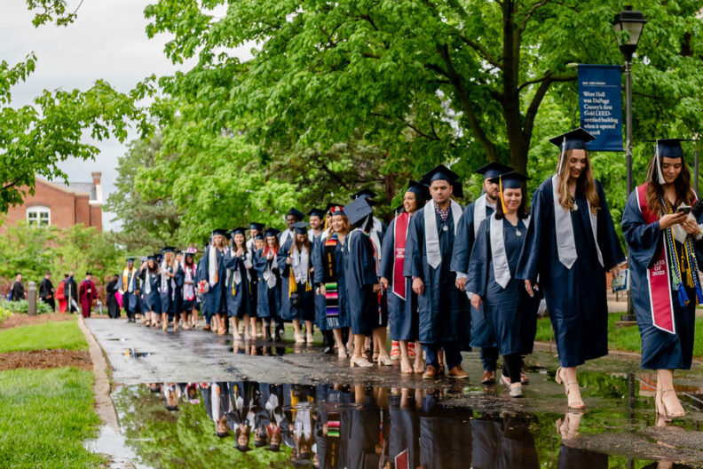A line of students in graduation caps and gowns walks toward Elmhurst University's 2022 Commencement ceremony, preparing to graduate from the school.