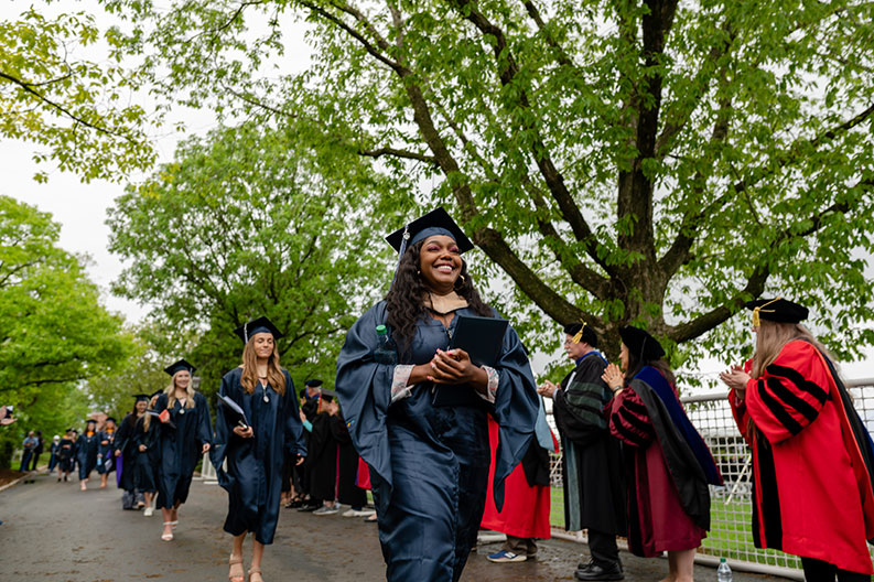 A smiling graduate student wearing cap and gown walks with other students at the end of Elmhurst University's 2022 Commencement ceremony.