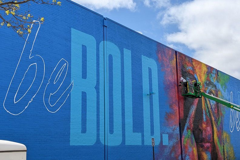 Elmhurst University art faculty member Rafael Blanco paints from atop a cherry picker, completing the mural "Be Bold. Be Elmhurst." on campus.