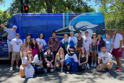 A group from Elmhurst University poses for a group photo before the 2022 Chicago Pride Parade, with an Elmhurst shuttle bus in the background.