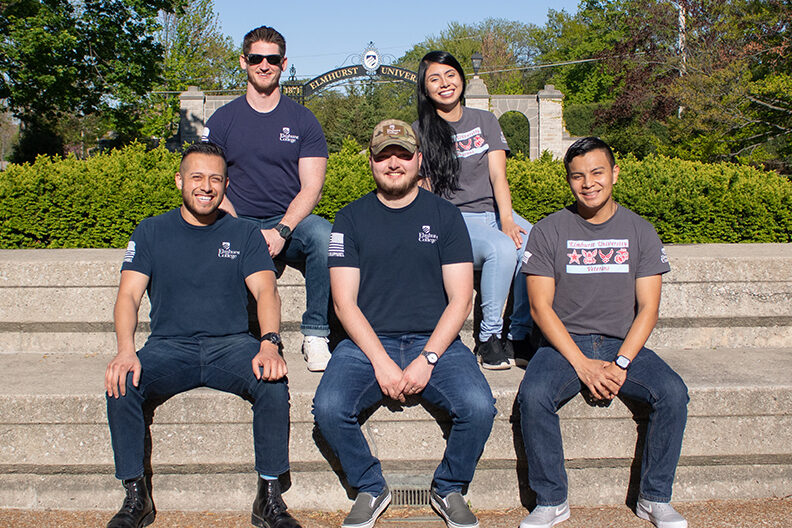 A group of five student-veterans sits on the steps of Elmhurst University's Kranz Forum.