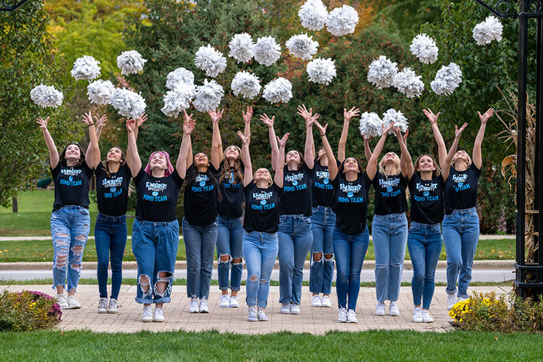 Members of the Elmhurst University Poms Team throwing their white poms up in the air.