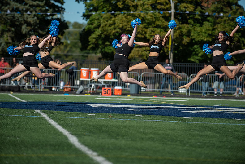 Dancers on the Elmhurst University Poms Team leaping during a performance at the 2022 Homecoming football game.