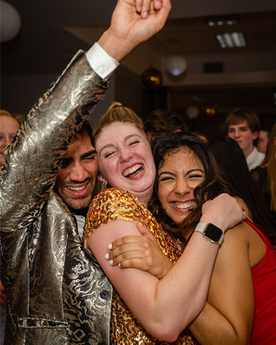 A male and two female Elmhurst University students hug on the dance floor during the Presidents' Ball event.