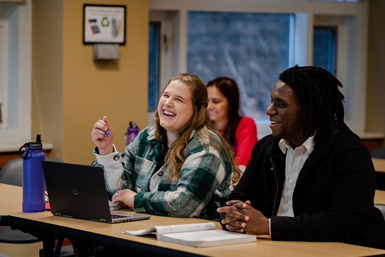 Two Elmhurst University education students smile while sitting next to each other in a class.