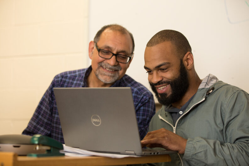 An Elmhurst University graduate student in Computer Information Technology laughs while Prof. Ali Ghane points to a computer screen.