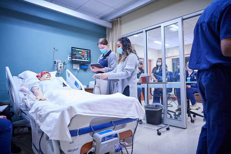 Two nursing students stand over a hospital bed with a mannequin serving as the patient for training purposes in the University's Simulation Center.