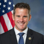 Former Illinois Congressman Adam Kinzinger standing in front of the American flag.