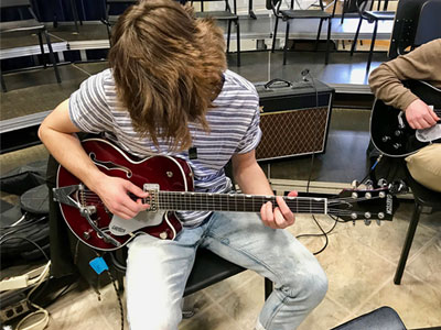 A male Elmhurst University student playing an electric guitar.