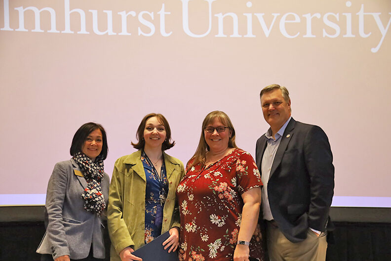 Four people stand in front of Elmhurst University background