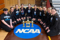 group of girls sitting around NCAA seal with trophies