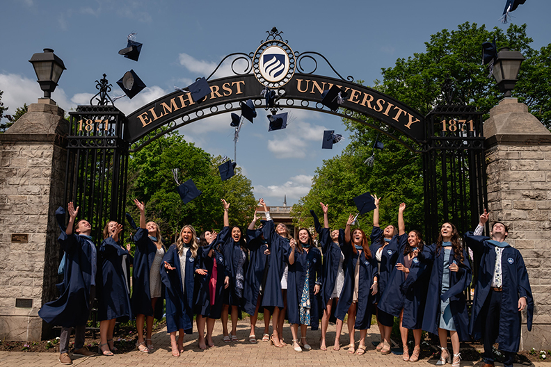 Graduates throwing their caps in front of the Elmhurst University gates