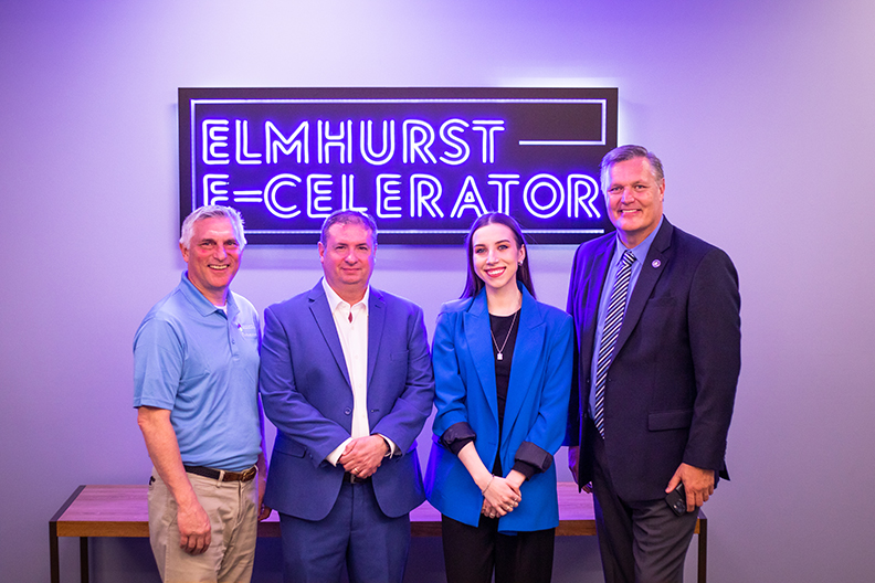 Four people standing in front of neon sign reading ELMHURST E-CELERATOR